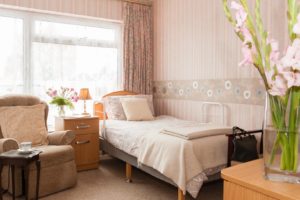 Residents room with single bed, furniture, flowers and striped wallpaper